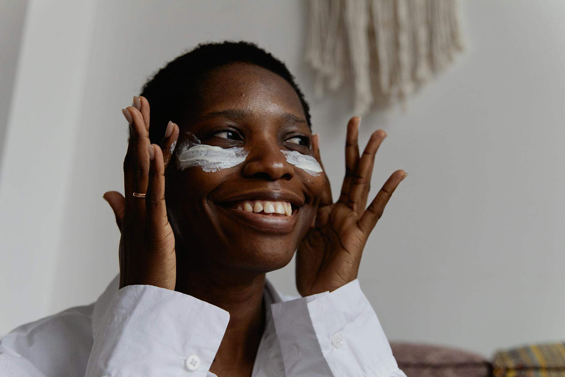 Czarnoskóra kobieta z uśmiechem nakłada krem na twarz w domu