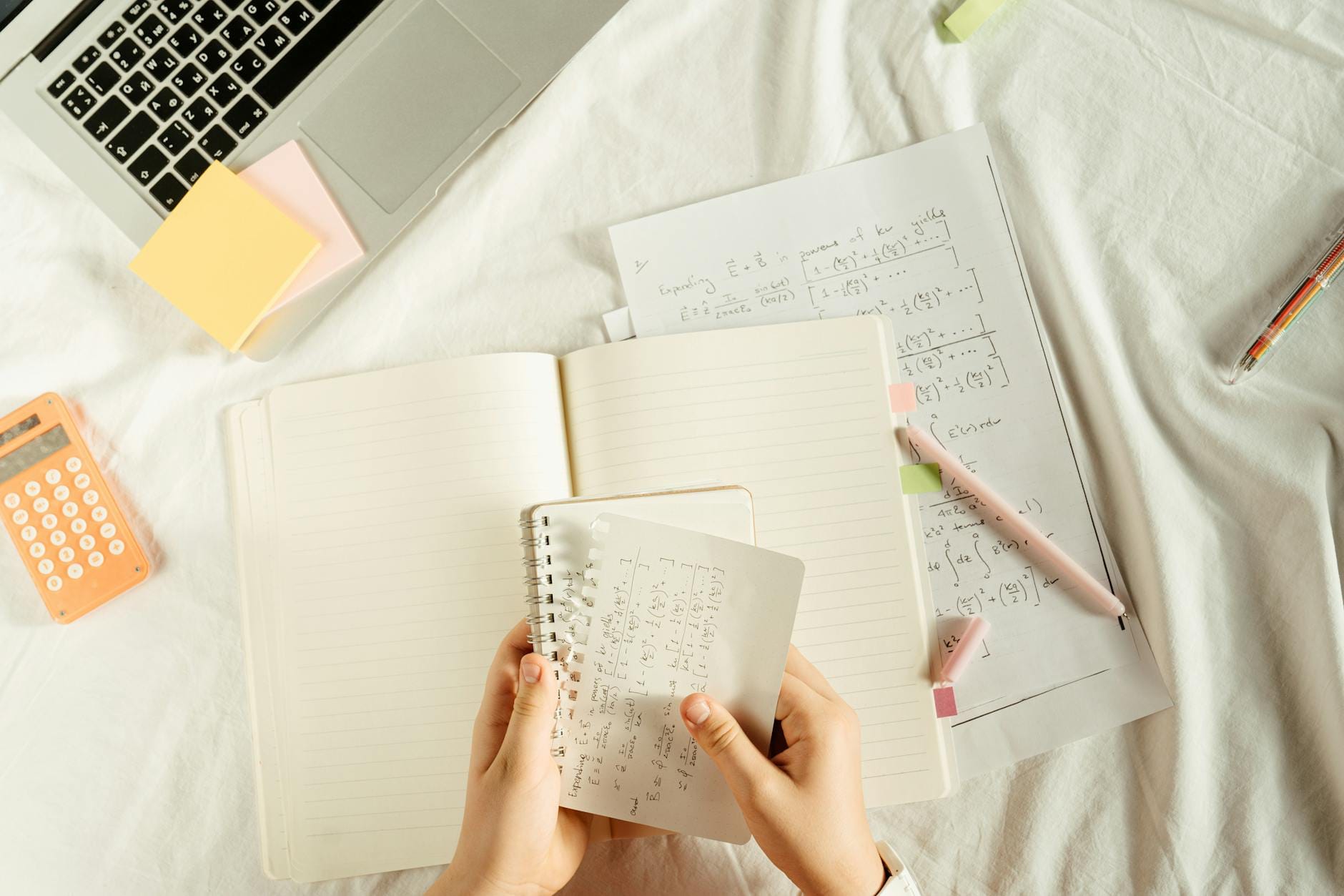 Uczeń uczy się matematyki przy biurku z zeszytem, kalkulatorem i laptopem