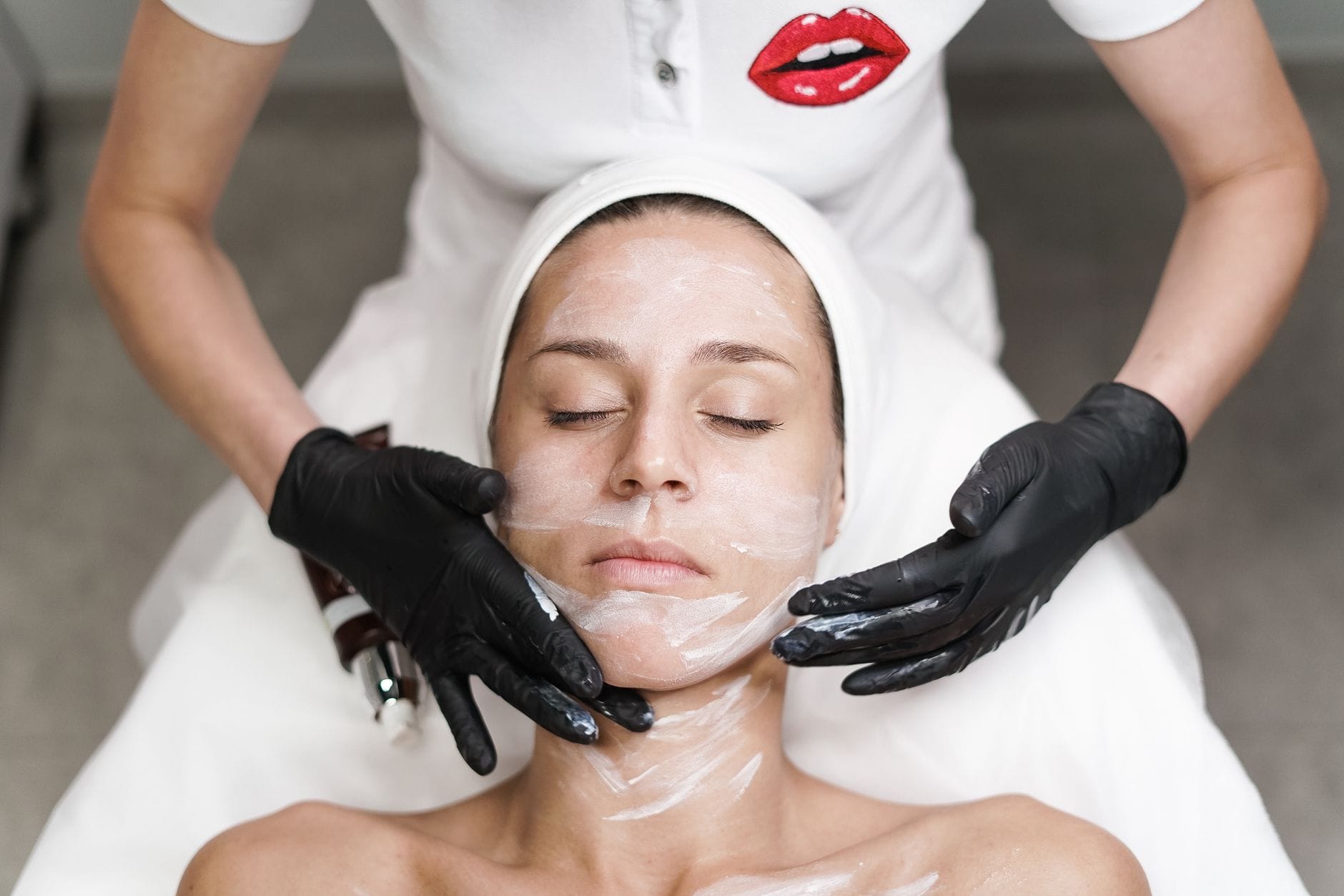 Kobieta podczas zabiegu na twarz w spa, kosmetyczka nakłada maskę