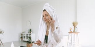 Kwas migdałowy w letniej pielęgnacji – czy powoduje przebarwienia posłoneczne? Kobieta w szlafroku nakłada kosmetyk do pielęgnacji twarzy w łazience